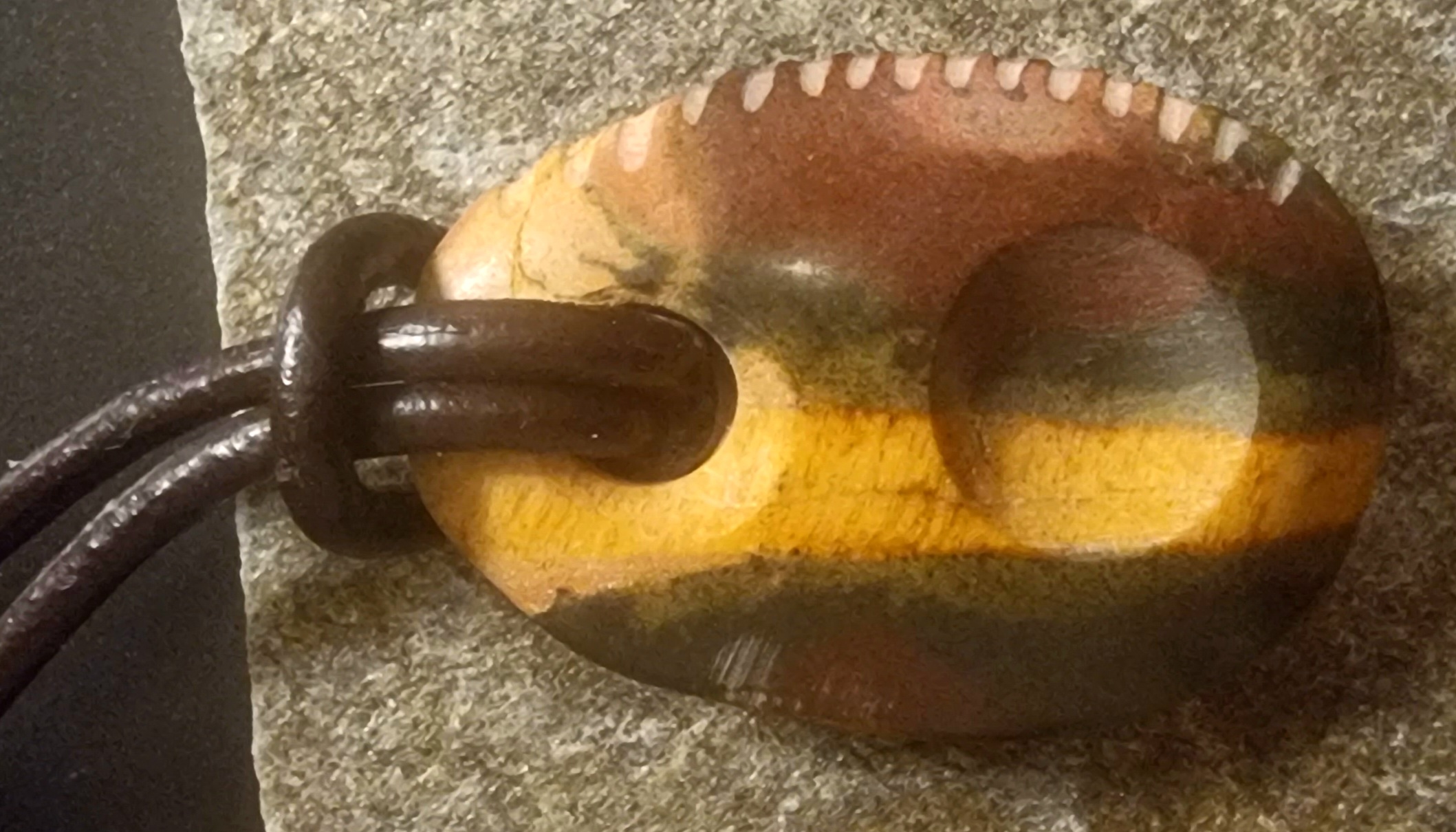 ovale steen met rood, geel en groene kleurbanderingen en gekartelde rand en een touwtje